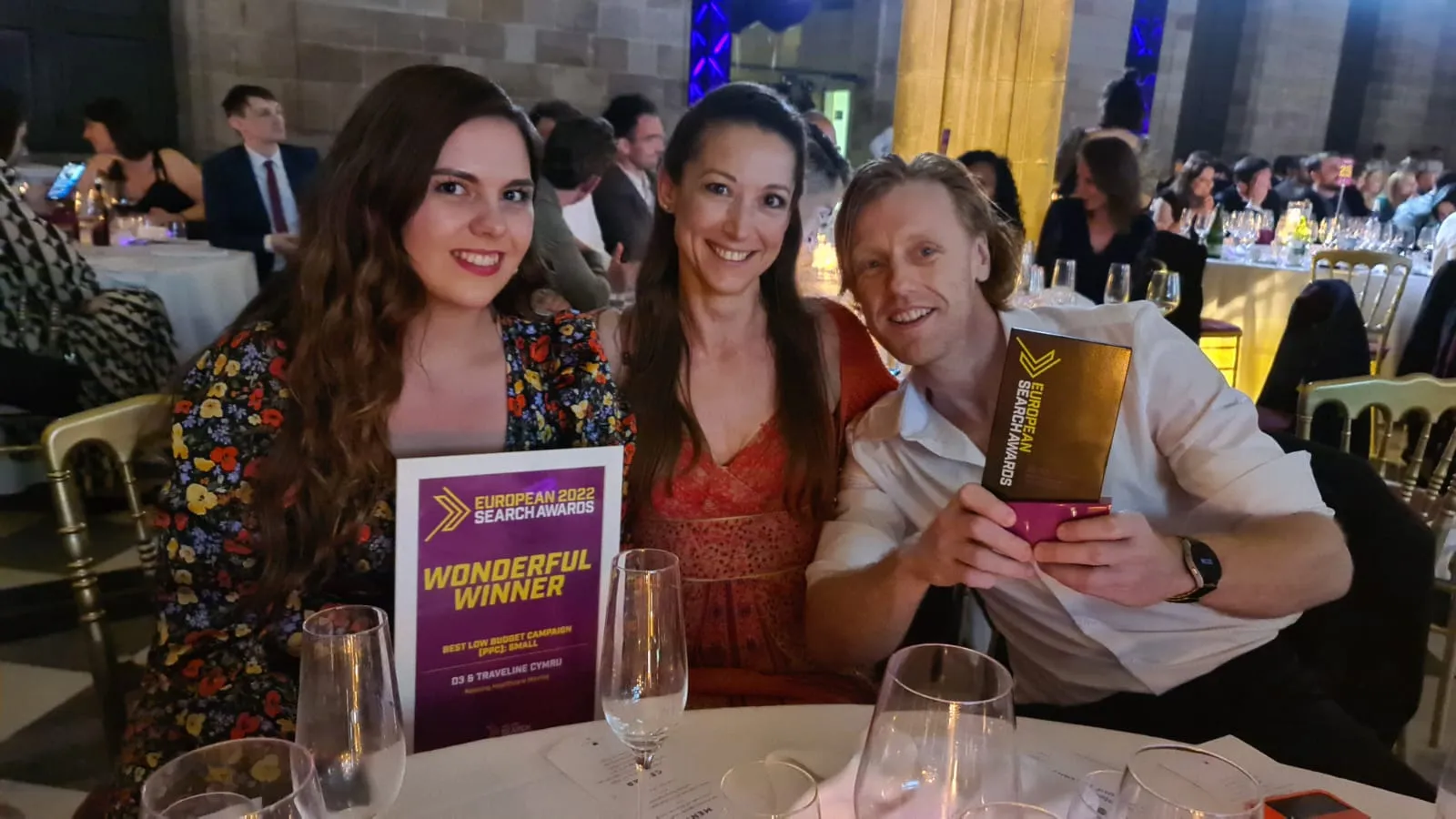 Kate Horsington, Luke Maggs and Ellie Jerman of Traveline Cymru at their table at the 2022 European Search Awards in Barcelona, holding the trophy and the winner's card